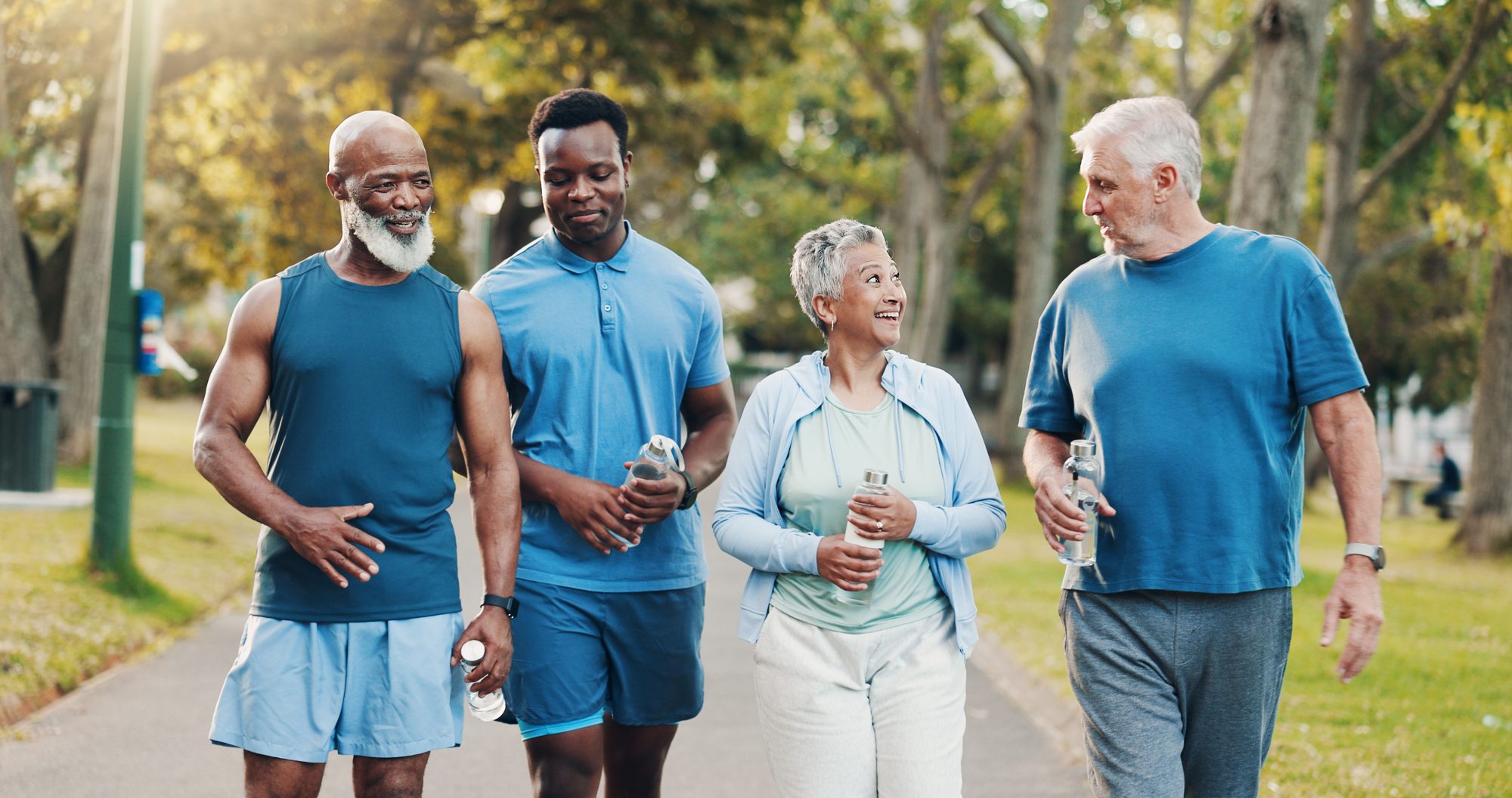 Four adults in their 50s and 60s walking and chatting on a sunny park path