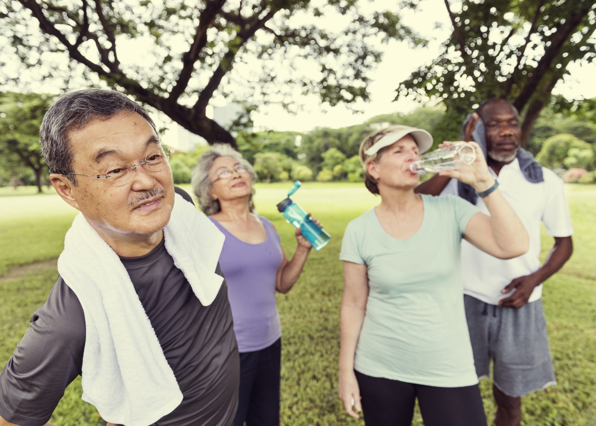 Four adults taking a water break after exercise in a park